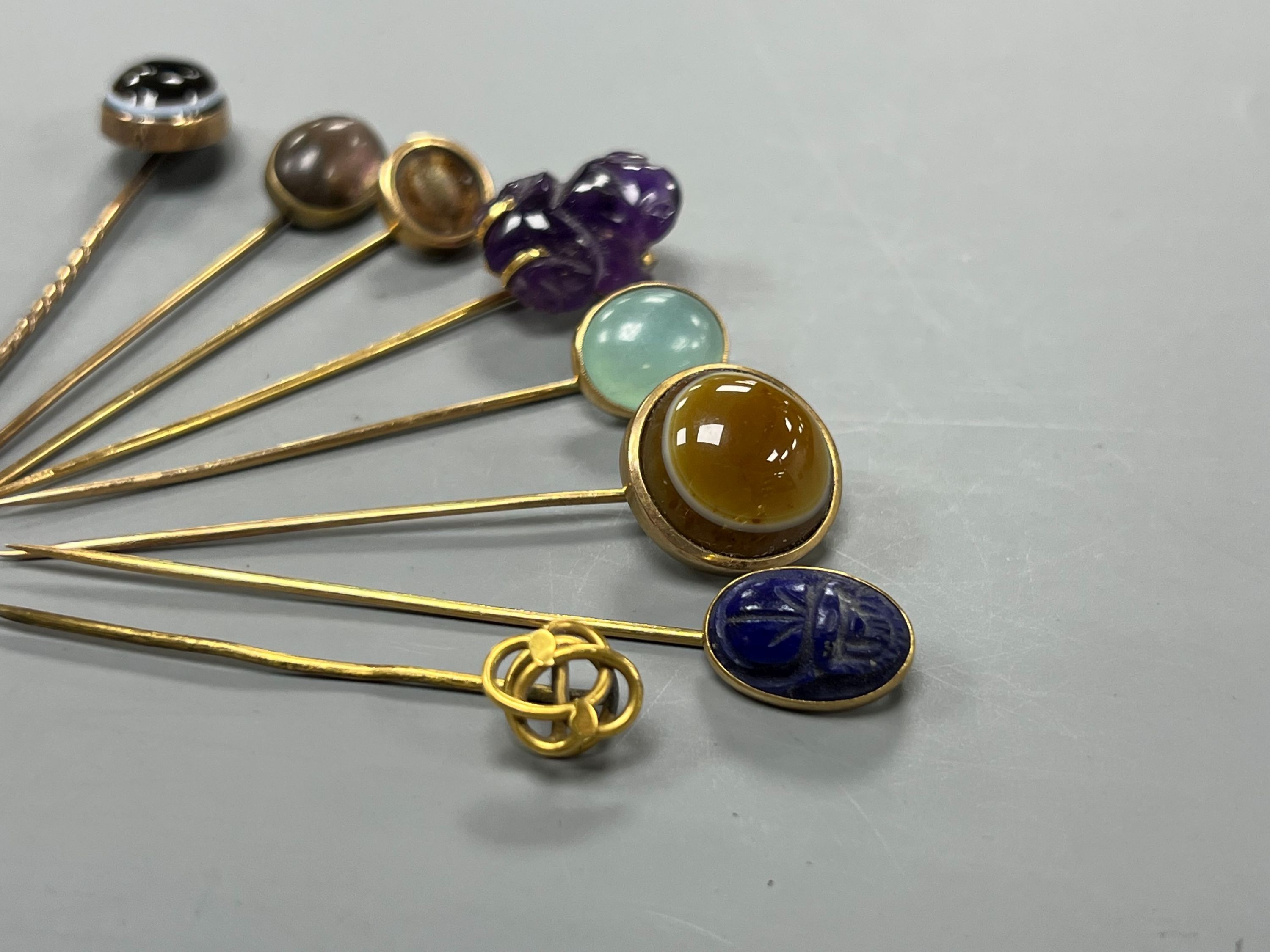 A small collection of eight assorted mainly yellow metal and chalcedony set stick pins, including Scarab, amethyst frog and banded agate